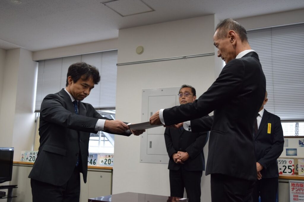 日本郵便の五味執行役員㊧に処分書を手渡す東運支局の織田支局長